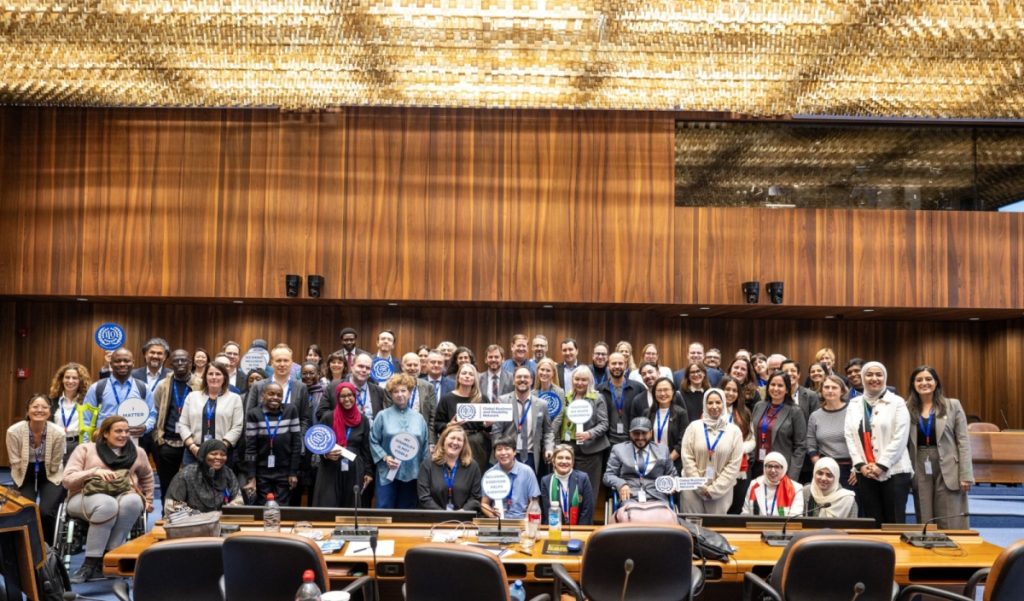 Zdjęcie grupowe uczestników konferencji ILO Global Business and Disability Network w Genewie. W sali konferencyjnej Międzynarodowej Organizacji Pracy ponad 60 osób z różnych krajów, w tym osoby z niepełnosprawnościami.