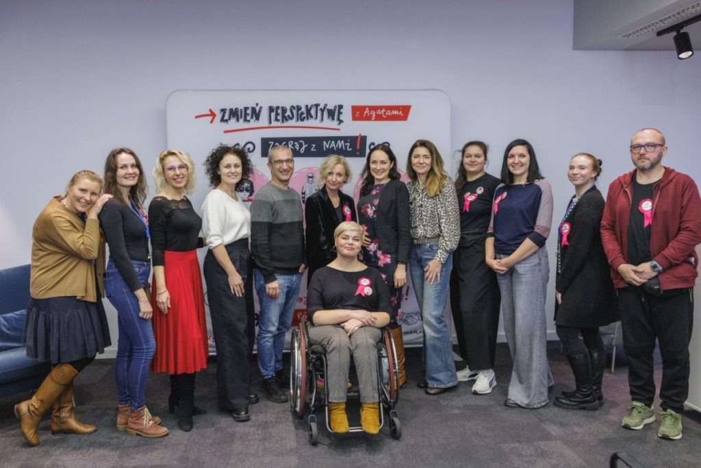 Czternaście osób pozuje wspólnie na tle planszy z napisem „Zmień perspektywę z Agatami”. W centrum kobieta na wózku, obok Agata Robińska i członkowie Zespołu na TAK. Większość osób ma różowe przypinki z napisem „Zmień perspektywę”.