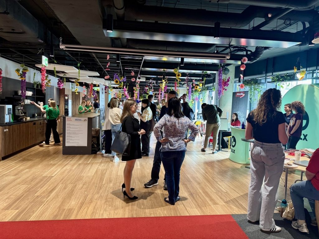 Participants and company representatives talking at employer stands during the Job Fair. In the background: OLX and Miele logos, colourful decorations, and a staffed coffee point.