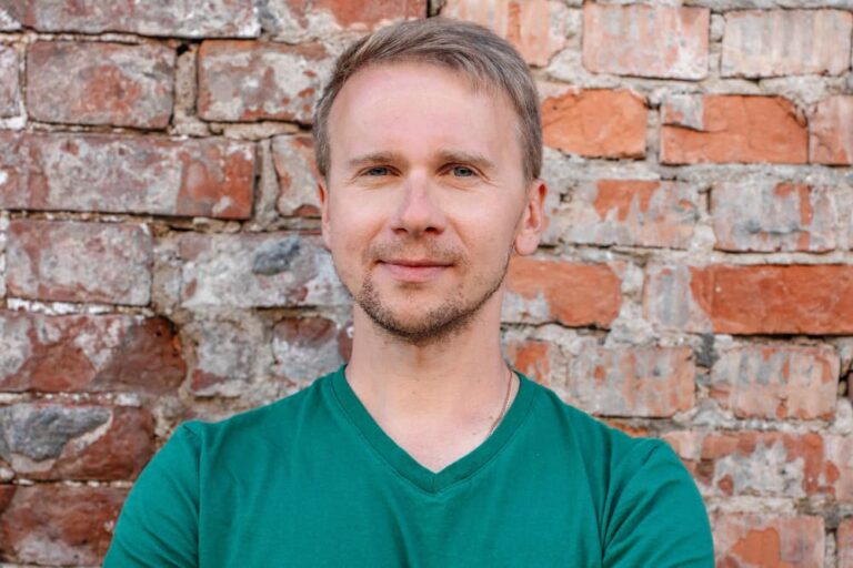 Mężczyzna w zielonej koszulce przed ceglaną ścianą.